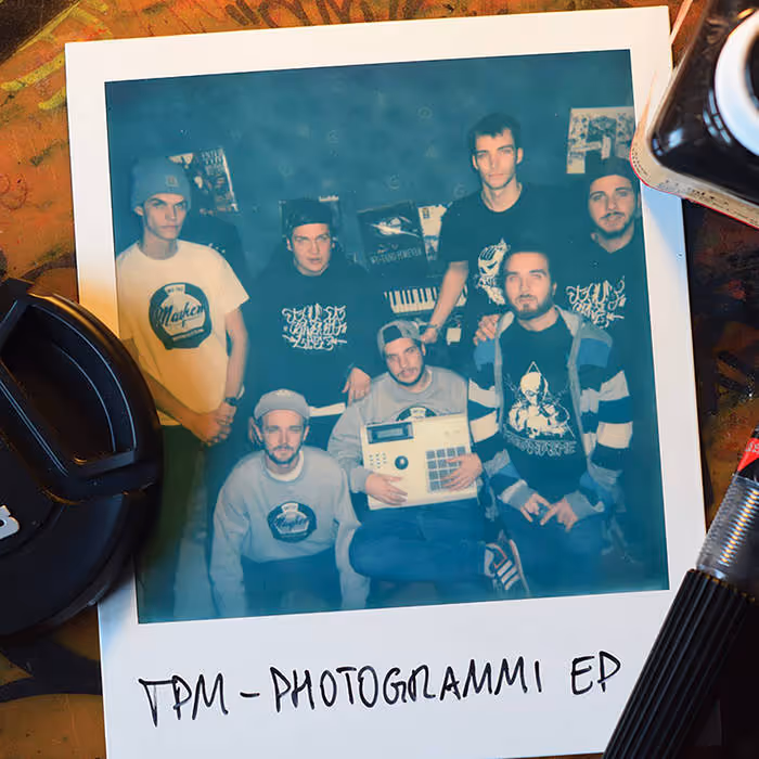 Polaroid photo of six men posing indoors with music equipment, captioned 'TPM - PHOTOGRAMMI EP.'